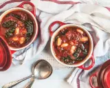 Due ciotole rosse con zuppa di cavolo nero, fagioli e pomodoro, pronte per essere gustate.