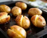 Plusieurs pommes de terre au four, dorées et fendues, sur une plaque de cuisson.