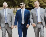 Groomsmen in grey suits and patterned ties walk together, showcasing stylish wedding pocket square folds.