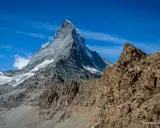 Majestatyczny Matterhorn wznosi się na tle błękitnego nieba. Widok zapiera dech w piersiach, sugerując trudne wejście na Matterhorn.