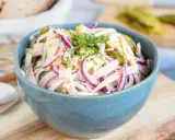 Schmackhafter schweizer wurstsalat mit roten Zwiebeln und Käse in einer blauen Schüssel, garniert mit Petersilie.