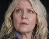 En kvinna med blont hår och blå ögon, klädd i lila, ser oroligt ut. Kanske är hon mitt i ett dramatiskt ögonblick i **shetland serie**.