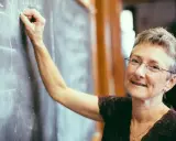 Lehrerin schreibt an Tafel. Was verdient ein Gymnasiallehrer? Sie lächelt wissend.