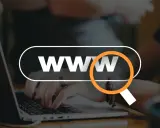 Dłonie piszące na laptopie, z lupą nad napisem "WWW".