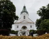 Biały kościół z zegarem na wieży, otoczony drzewami. Zastanawiasz się, jak sprawdzić do której parafii należę?