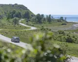 En bil kör på en slingrig väg längs Gotlands kust. Perfekt för att upptäcka nya aktiviteter på Gotland.