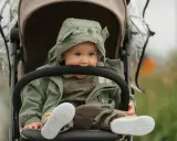 Maluch w wózku, w zielonej kurtce z misiem, gryzie pałąk. To urocze babciowe chwile.