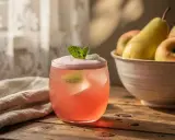 Verre de boisson rose pétillante, garni de menthe. Un bol de fruits et un tissu sont en arrière-plan. Délicieux eau de rhubarbe.