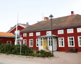 Röda trähus med vita fönster och tegeltak. En skylt visar "Stiftsgården Undersvik". Vackert beläget med natur och vatten i bakgrunden.