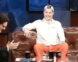 Zabson, z uśmiechem na twarzy, siedzi na kanapie w studiu. Obok niego siedzi mężczyzna w okularach.