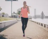Frau joggt am Fluss entlang. Sie beweist, dass ist joggen gesund und ein toller Start in den Tag.