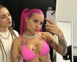 Dwie młode kobiety, jedna z różowymi włosami i tatuażami, druga z warkoczami, pozują do selfie.