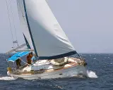 Voile blanche gonflée par le vent, le voilier avance sur la mer bleue. La bosse de ris sur la grand-voile est visible, signe d'une navigation par vent fort.