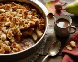 Un délicieux crumble poire chocolat, garni de noix et de morceaux de chocolat, prêt à être dégusté avec une sauce onctueuse.