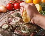 Fleisch marinieren für den Grill: Zitrone über mariniertes Fleisch mit Zwiebeln und Kräutern ausdrücken.