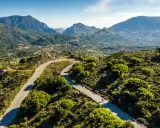 Ein Rennradfahrer auf Kreta genießt die kurvenreiche Straße durch eine grüne Berglandschaft.