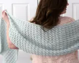 Mujer con chal rectangular de crochet azul claro sobre vestido rosa.