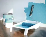 Latas de pintura plástica acrílica y rodillo listo para dar vida a una pared azul.