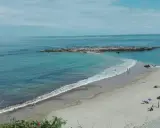 La **playa de Pechón** se extiende con arena dorada y aguas turquesas. Unas rocas emergen del mar, mientras algunas personas disfrutan del sol y el mar.