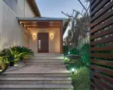 Un portico moderno con porta in legno scuro, illuminazione soffusa e piante rigogliose. Un esempio di come abbellire un portico con stile e natura.