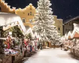 Mercatini di Natale nel Nord Italia, con bancarelle innevate, un grande albero illuminato e case decorate. Magia invernale.