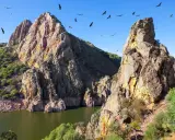 Felsige Berge und ein Fluss in Extremadura, Spanien. Geier kreisen am blauen Himmel über der rauen Landschaft.
