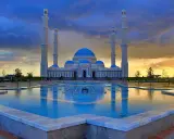 Die Hazrat-Sultan-Moschee in Astana, ein architektonisches Meisterwerk, spiegelt sich im Wasser eines Brunnens unter einem dramatischen Abendhimmel.