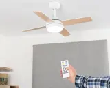Mano con mando a distancia operando un ventilador de techo escayola con luz integrada.