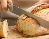Krojenie świeżo upieczonego bochenka, idealnego na domowy przepis na chleb pieczony w piekarniku. Chrupiąca skórka i miękki środek.