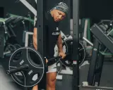 Mann im Fitnessstudio bereitet sich auf schwere myo reps vor, hält eine Langhantel mit 20kg Scheiben.