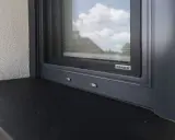 Detale montażu parapetów zewnętrznych. Ciemny parapet pod szarym oknem z moskitierą.