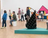 Visitors explore diverse artworks in what is an art gallery, from video installations to abstract sculptures and colorful wall art.