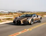 Ein bronzener Bugatti Mistral fährt auf einer Küstenstraße.
