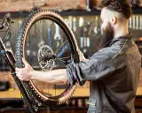 Mechanik z brodą sprawdza oponę gravelową roweru. Zastanawia się, ile mleka do opony gravel będzie potrzebne, by zapewnić najlepszą przyczepność.