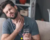 Mężczyzna z bólem gardła, trzymający szklankę wody, szuka sposobu, jak pozbyć się drapania w gardle.