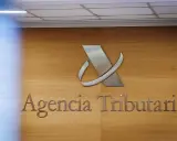 Logo y nombre de la Agencia Tributaria en una pared de madera.