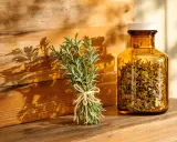 Un bouquet de romarin frais et une fiole ambrée remplie de feuilles séchées, évoquant le bienfait romarin pour la santé et le bien-être.