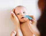 Mama delikatnie oczyszcza nosek niemowlaka z katarem za pomocą aspiratora.