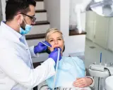 Dentysta wykonuje piaskowanie zębów u pacjentki, która siedzi na fotelu dentystycznym.