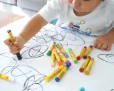 Bambino disegna con pastelli su foglio bianco. I disegni dei bambini sono un modo per esprimere emozioni, ma quando preoccuparsi?