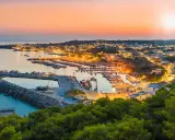 Porto illuminato al tramonto, un invito al turismo Salento. Barche ormeggiate e case che brillano sulla costa.