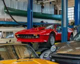 Taller mecánico con autos clásicos: un rojo Ferrari en elevador, un Porsche gris y un amarillo. ¡Ideas para tu taller!