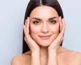 Mujer con piel radiante, resultado del colágeno para la piel. Sus manos acarician su rostro, mostrando una tez suave y luminosa.