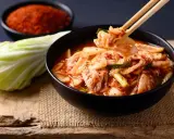 Miseczka z kimchi, pałeczki podnoszące kawałek kapusty, obok kapusta i miseczka z przyprawą.