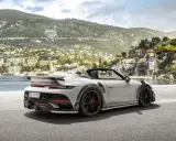 Ein weißer Techart GTstreet RS Cabriolet steht an einer Küstenstraße mit Blick auf eine malerische Stadt am Hang.