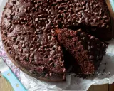 Torta al cioccolato senza uova, soffice e golosa, ricoperta di gocce di cioccolato. Una fetta mostra la sua morbidezza.