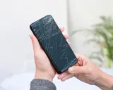 Dłoń trzyma pęknięty telefon, czekając na wymianę ekranu.