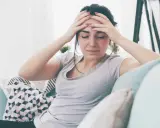 Kobieta z rękami na skroniach, wyrażająca ból głowy, być może objaw psychosomatyki.