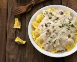 Ravioli w kremowym sosie śmietanowym z grzybami i natką pietruszki, podane na drewnianym stole.