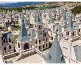 Un villaggio di case a forma di castello, Burj Al Babas, con tetti a punta grigi e facciate bianche, immerso in un paesaggio collinare.